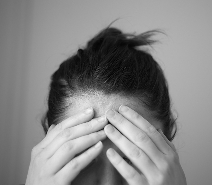 a grayscale photo of the upper half of a woman's head with her hands touching her forehead